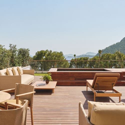 Eine geräumige Außenterrasse mit Holzdeck, ausgestattet mit Liegestühlen, einem Sofa, einem runden Tisch mit Stühlen und einem rechteckigen Tauchbecken, mit Blick auf eine malerische Landschaft mit Bäumen und einem Berg unter klarem Himmel.