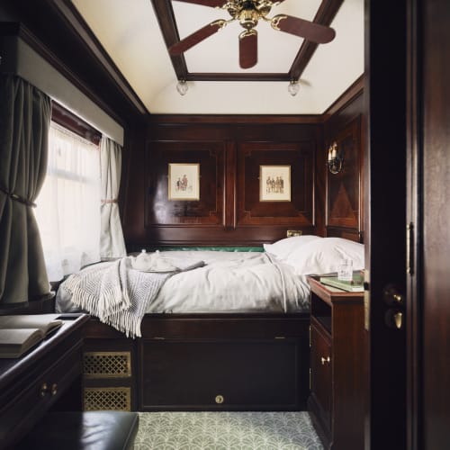 Cozy bedroom with dark wooden wall paneling, a single bed with white bedding, and a ceiling fan in a luxurious setting.