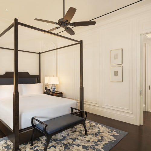 Elegantes Schlafzimmer mit einem Himmelbett aus dunklem Holz, in einer luxuriösen Suite mit weißen Wänden, Deckenventilator und klassischer Dekoration.