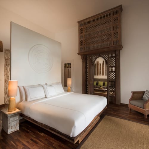 Ein geräumiges, elegant dekoriertes Schlafzimmer mit einem großen Bett, Holzmöbeln und ethnisch inspirierten Dekorationen im Raum.