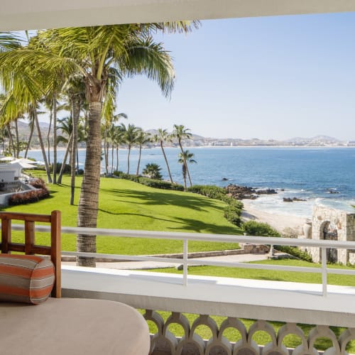 Blick von einem Balkon auf einen tropischen Strand mit Palmen, grünem Rasen und dem Meer im Hintergrund.