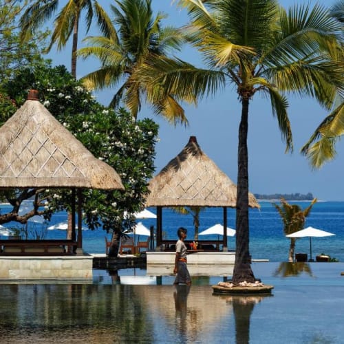 Schwimmbad mit Blick auf den Strand, mit strohgedeckten Hütten und Palmen am Oberoi Beach Resort, Lombok.