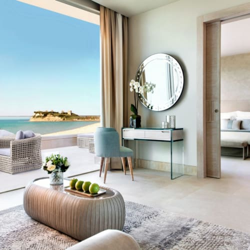 Luxuriöse Strand-Suite mit großem Wohnbereich mit Blick auf das Meer, ausgestattet mit moderner Einrichtung, einem großen Spiegel und großen Balkonüren.