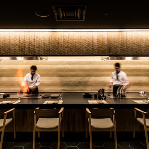 Zwei Köche bereiten Essen hinter einer Theke in einem modernen Restaurant mit elegantem Design vor.