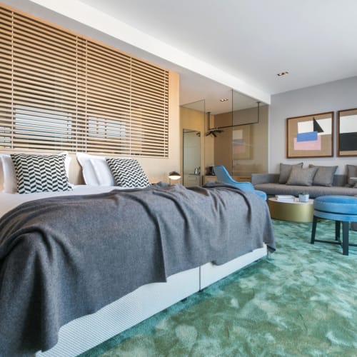 Luxuriöse Hotel-Suite mit großem Bett, modernem Dekor und Sitzecke in einem hellen Raum.