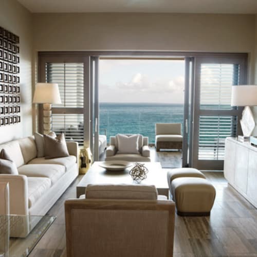 Luxuriöses Wohnzimmer mit Meerblick, mit weißen Sofas, Sesseln, einem Glastisch und Schiebetüren, die zu einem Balkon mit Blick auf das Meer führen.