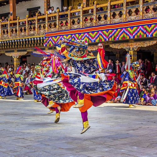 Traditionelle bhutanische Tänzer in bunten Kostümen führen einen Tanz in einem offenen Hof während eines Festivals in Punakha auf.