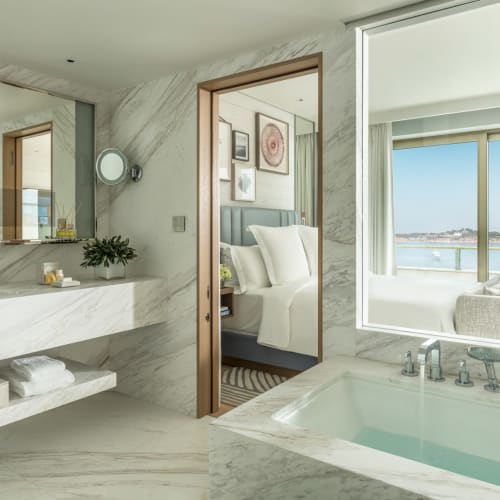 Luxuriöses Badezimmer mit großer Badewanne mit Blick auf einen Balkon mit Wasserblick in einer Hotel-Suite.