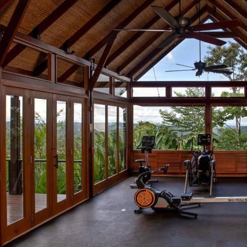 A spacious indoor fitness area with large glass windows and a view of lush green trees and plants.