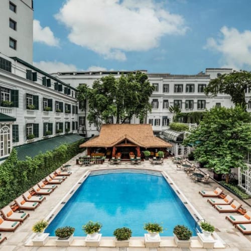 Ein Swimmingpool in einem Hotelgarten mit Liegestühlen und Palmen im Hintergrund.