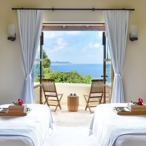 Zwei Betten in einem hellen Raum, der zu einem Balkon mit Meer- und Grünblick führt.