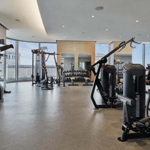 Modernes Fitnessstudio mit verschiedenen Trainingsgeräten wie Laufbändern, Gewichten und Maschinen mit Blick auf die Stadt durch große Fenster.