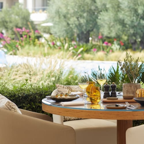 Ein Außentisch mit Essen und Wein, umgeben von Pflanzen, mit Blick auf einen gepflegten Garten.