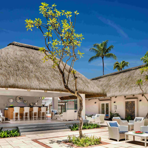 Luxushotel in Mauritius mit Strohdach-Lounges und Sitze im Freien unter einem klaren blauen Himmel.