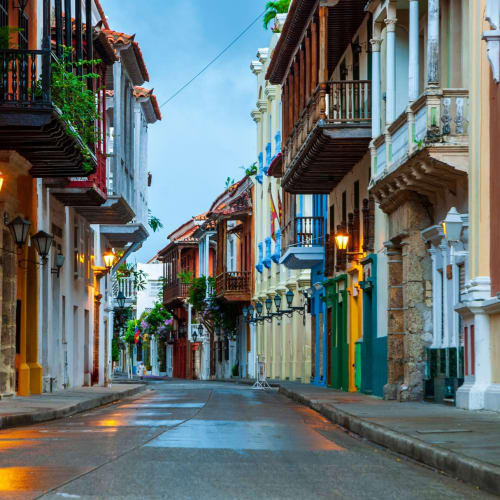 Bunte Kolonialgebäude säumen eine ruhige Straße in der Altstadt von Cartagena bei Dämmerung, mit leuchtenden Straßenlaternen.