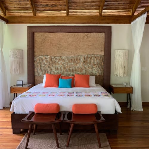 Luxurious bedroom with a large bed, colorful pillows, and wooden furniture in a rustic room.