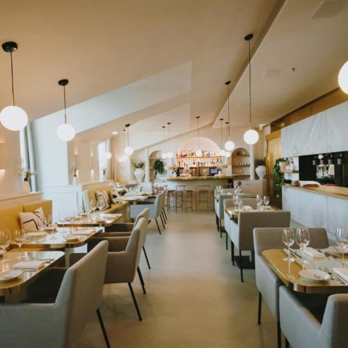 Innenraum eines modernen, gut beleuchteten Restaurants mit weißen Wänden, hängenden runden Lichtern und gepflegten Tischen mit Glaswaren und Besteck.