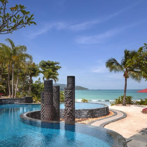 Luxuspool mit Blick auf einen tropischen Strand mit Palmen und Sonnenschirmen in Seychellen