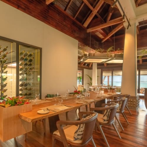 Elegant dining area in a modern restaurant with large windows, wooden floors, and a glass wine display.