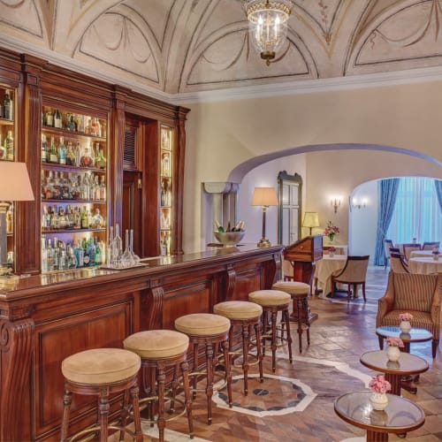 Elegante Hotelbar mit einer hölzernen Theke, gut gefüllter Spirituosenregalung und komfortabler Sitzgelegenheiten in einem luxuriösen Ambiente.