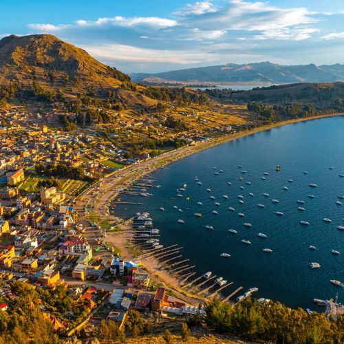 A panoramic view of Copacabana town along the shores of Lake Titicaca with boats and hills in the background.