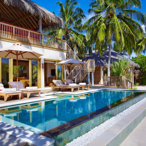 Luxusvilla mit Außenpool, umgeben von Palmen in einem tropischen Resort.