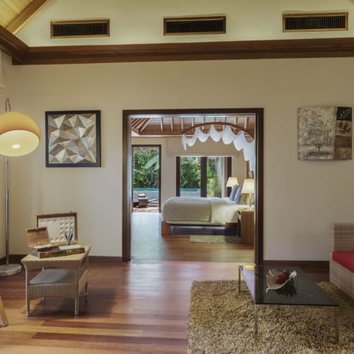 Das Wohnzimmer einer luxuriösen Villa mit modernem Dekor, Holzboden, einem Sofa mit Kissen und einer Öffnung, die zu einem Schlafzimmer im Hintergrund führt.