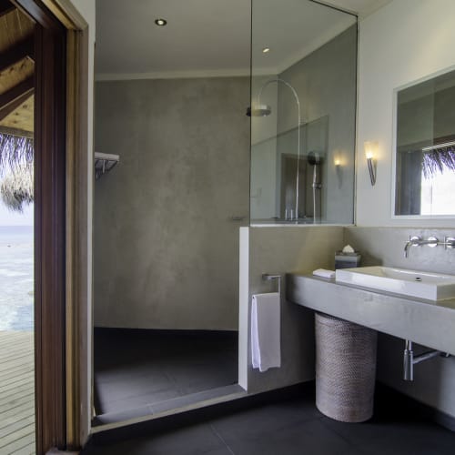 Modernes Badezimmer mit Blick auf den Ozean, mit begehbarer Dusche und großem Spiegel in einer Wasser-Villa.