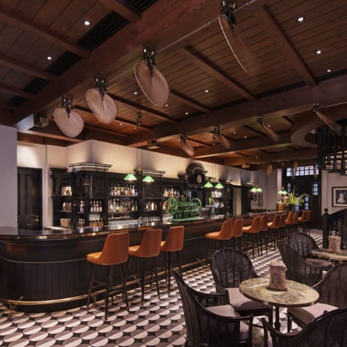 Luxurious bar interior with a curved black counter, orange bar stools, and black wicker chairs around small tables in a sophisticated setting.