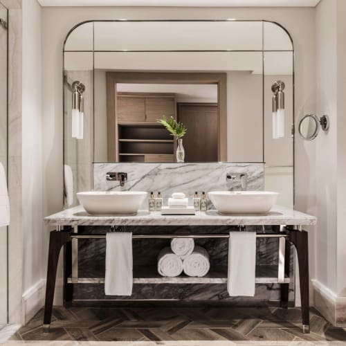 Elegantes Badezimmer mit Doppelwaschbecken und großem Spiegel, der eine dekorative Vase widerspiegelt.