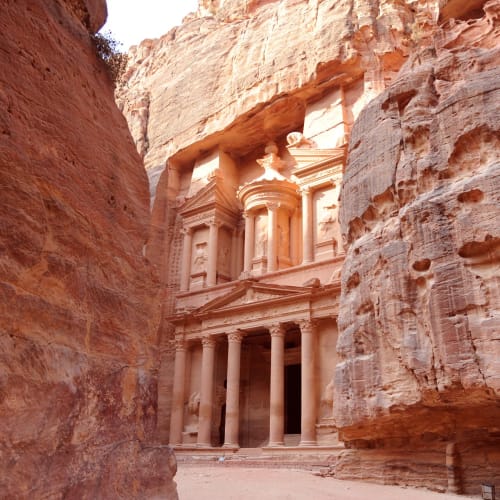 The historic facade of the Treasury in Petra, Jordan, visible through a narrow canyon.