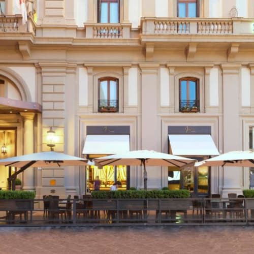 Outdoor terrace with chairs and umbrellas outside the Rocco Forte Hotel Savoy in Florence.