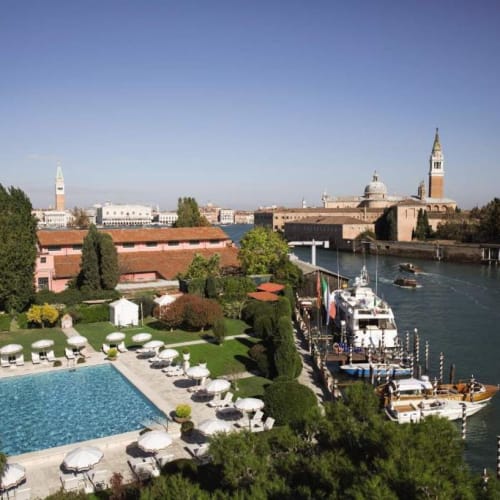 Ein Blick auf den Außenpool und den Garten des Hotel Cipriani in Venedig, mit der Skyline und dem Fluss im Hintergrund.