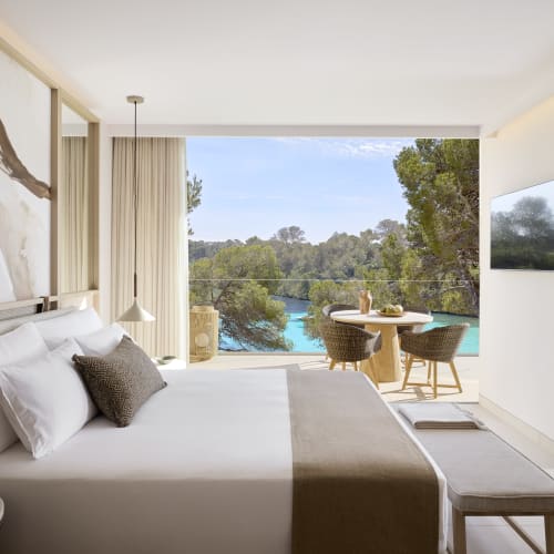 Bright and modern hotel room with a large bed, overlooking a balcony with a scenic sea view and outdoor dining area.