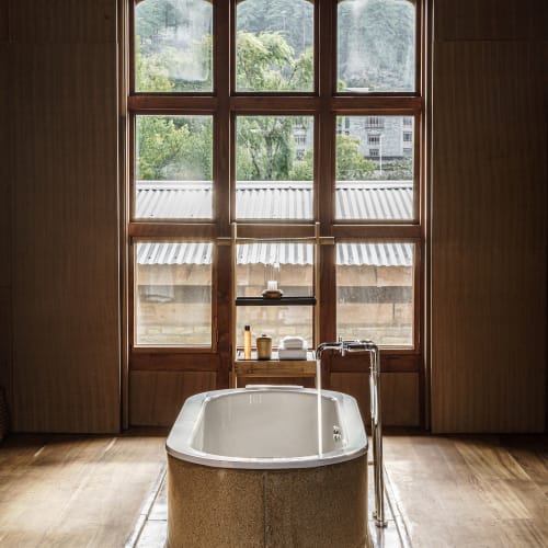 Eine moderne Badewanne vor einem großen Fenster mit Holzrahmen, das grüne Natur und Berge in Bhutan zeigt.