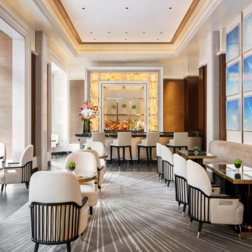 Elegantes Café- oder Restaurantinnenraum mit großen Fenstern, weißen Stühlen und gerahmter Kunst an der Wand.