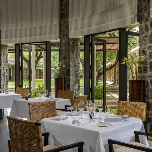 Elegantes Restaurant-Innenraum mit Steinsäulen, großen Fenstern und ordentlich gedeckten Tischen mit weißen Tischtüchern und Glaswaren.