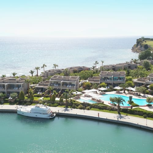 Luxury waterfront resort with a swimming pool, surrounded by modern villas and palm trees, overlooking the sea at Sani Marina.