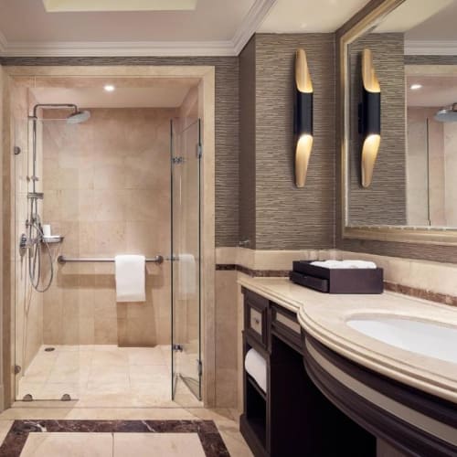 Ein modernes Badezimmer mit einer begehbaren Dusche, einem Waschbecken und Spiegeln, elegant gestaltet mit beige- und brauntönen.