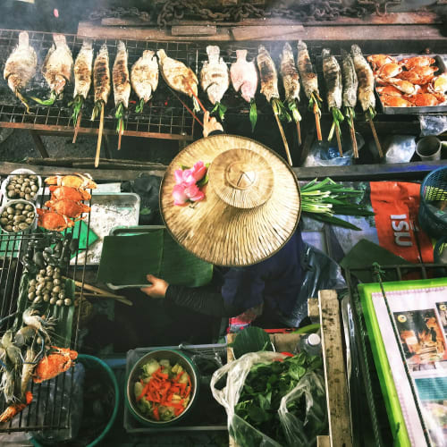 Street food stall in Bangkok, Thailand with grilled fish, seafood, and vegetables being prepared.