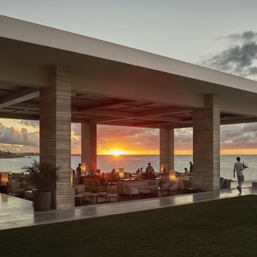 Ein Sonnenuntergangsausblick von einem Lounge-Bereich in einem Resort mit Sitzgelegenheiten im Freien und Blick auf den Ozean.