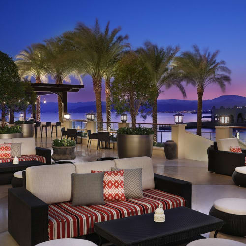 Ein stilvoller Außenbereich am Abend mit Palmen, modernen Möbeln und Blick auf das Wasser in Aqaba, Jordanien.