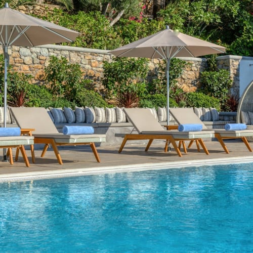 Luxuriöser Poolbereich mit Liegestühlen, Sonnenschirmen und einer gepolsterten Kabine in einer tropischen Umgebung.