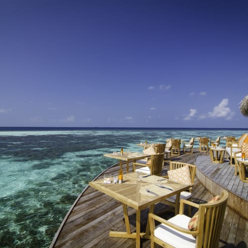 Außenrestaurant-Deck mit Holztischen und Stühlen mit Blick auf den klaren Ozean bei Mirihi, Malediven.