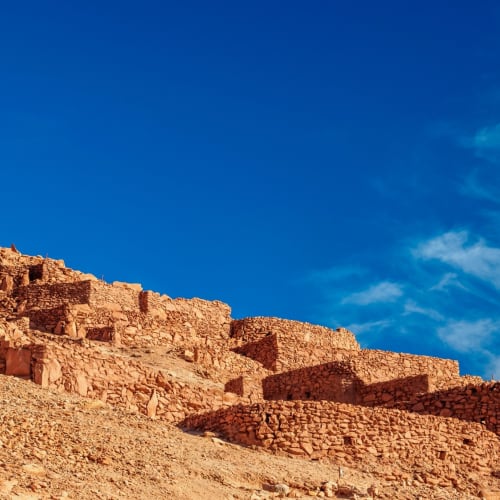 Ancient stone ruins built into a hillside against a blue sky in the Atacama Desert, Chile.