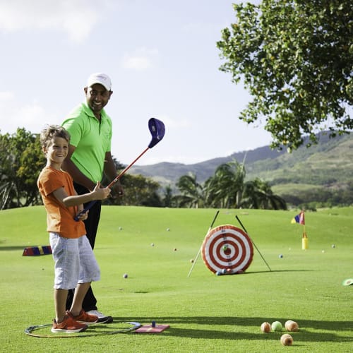 A family enjoying a game of golf on a lush green course with mountains and trees in the background.