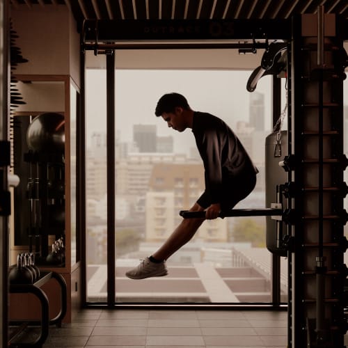 Ein Mann in einem Fitnessstudio, in einem Anzug, balanciert auf einer Stange vor einem großen Fenster mit Blick auf die Stadt.