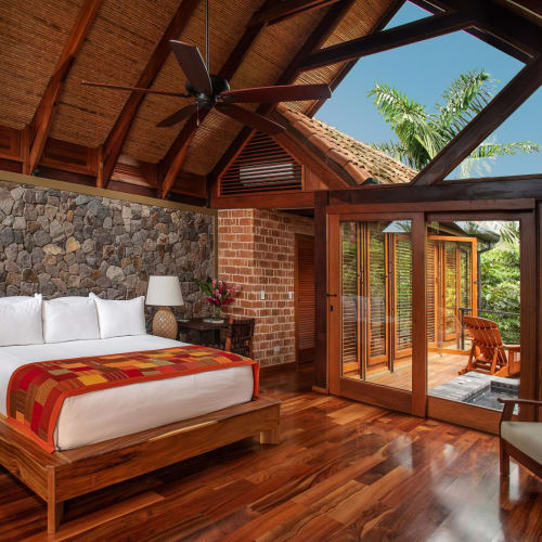 Bright, spacious bedroom with wooden floors, large windows, and a balcony overlooking lush greenery in Costa Rica.
