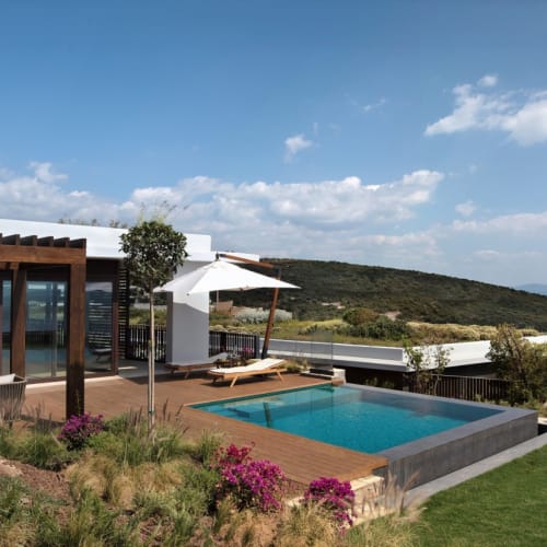 A luxurious outdoor area with a pool, seating, and a view of the sea and hills beyond.