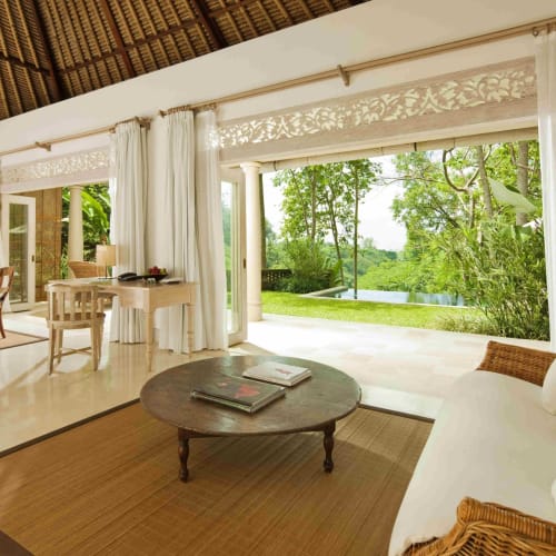 Lush green outdoor view visible from a spacious hotel room with white curtains and wicker furniture.